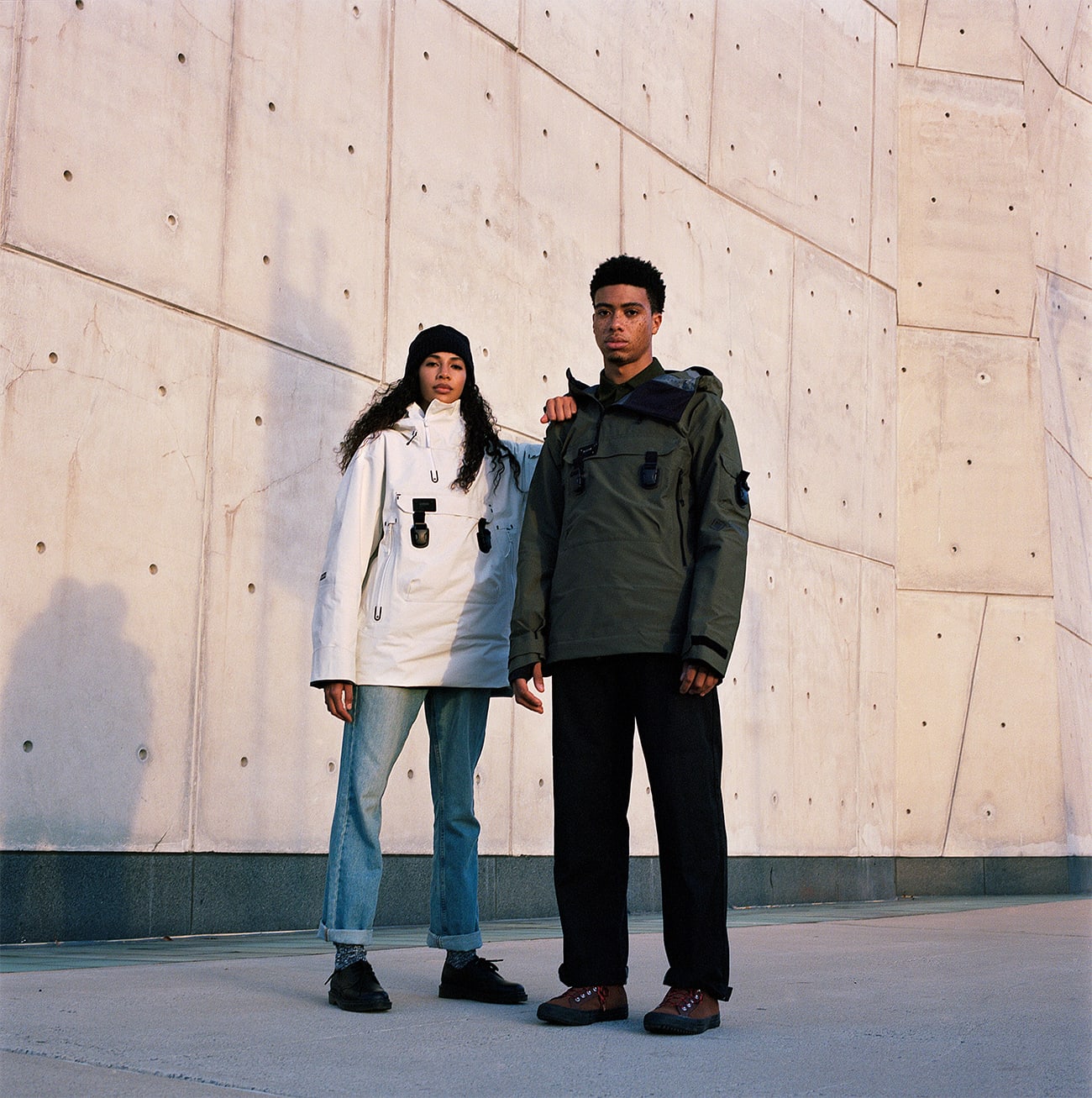 Models Julia Biango and Leron Nurse wearing Armada ski outerwear jackets, her jacket is white his jacket is army green. She is wearing a black hat. They are standing in front of a tall white building, her arm is on his shoulder. The male model has a lot of freckles. Look-book photographed by New York photographer Maria Bruun. The image was taken using the Hasselblad 500CM camera and Kodak Portra film.