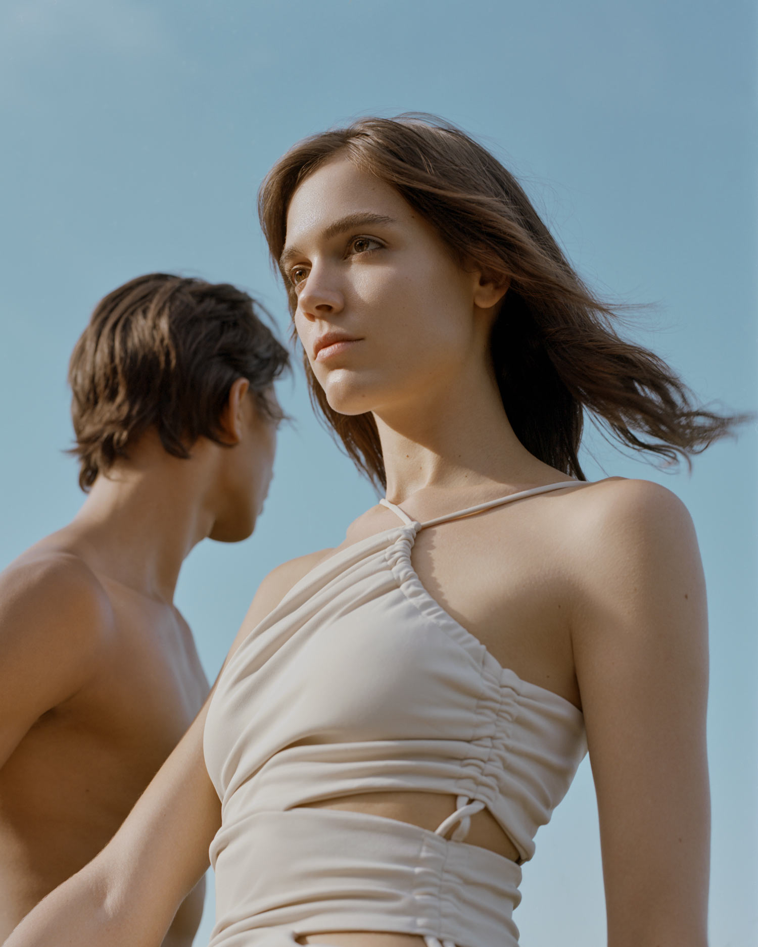 Female model Abby Blaine and male model Tyler Twitty, set against a blue sky, her hair is flowing in the wind. The sun is shining bright. she is wearing a beige Forever 21 dress, Photographed by New York photographer Maria Bruun, photographed using a Mamiya RZ67 camera and Kodak Portra 160 film.