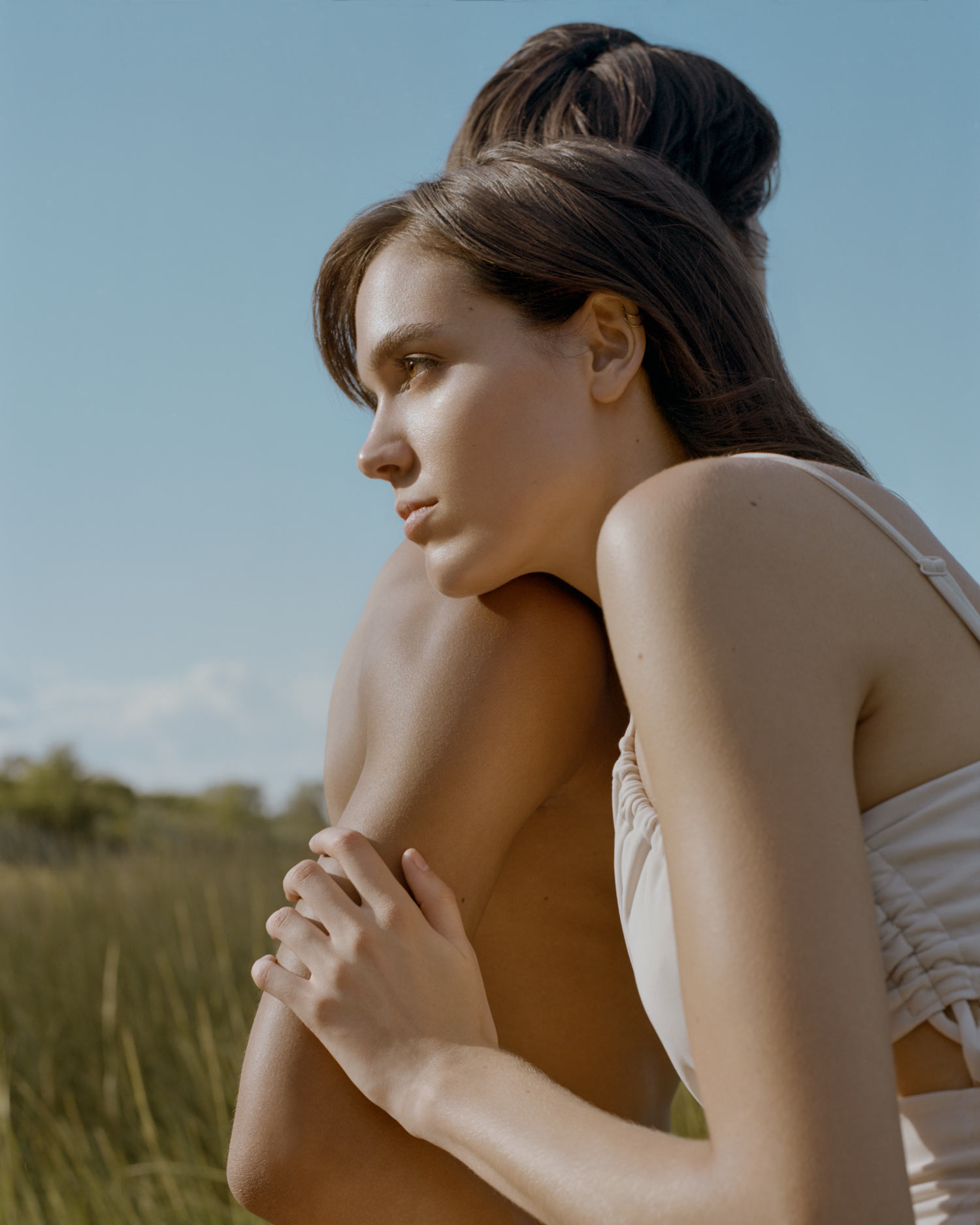 Female model Abby Blaine and male model Tyler Twitty, set against a blue sky and green grass. She is leaning on him. The sun is shining. she is wearing a beige Forever 21 dress, Photographed by New York photographer Maria Bruun, photographed using a Mamiya RZ67 camera and Kodak Portra 160 film.