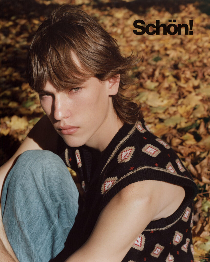 Color portrait of male model Luke Kitlen sitting in the grass surrounded by orange leaves, it is fall, he is wearing blue jeans and a black knitted sleeveless sweater. Location Liberty Harbor. Editorial for Schön! Magazine photographed by New York photographer Maria Bruun. Shot on film with the Mamiya RZ67 camera and Kodak Portra Film.